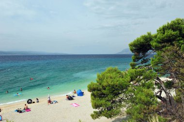 View over Makarska between Baska Voda and Brela in Croatia. Turquoise blue Adriatic ocean and people sunbathing on the beach. clipart