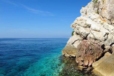 Karadağ 'ın Petrovac kentindeki Adriyatik Denizi üzerinde okyanus manzarası. Açık mavi gökyüzü ve turkuaz mavi su dağ yamacında.