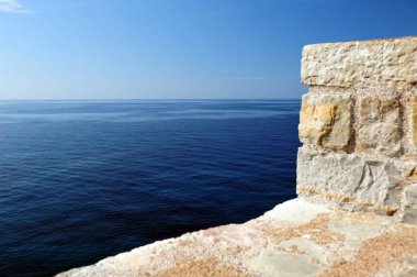 Adriyatik Okyanusu 'nun üzerinden beyaz tuğlalı çitlerin arkasına bak. Mavi deniz, açık gökyüzü. Kopya uzayı ile yatay çekim. Basit kompozisyon.