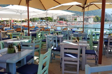 Petrovac restoranında gündüz vakti boş sandalye ve masalar. Plaj ve oteller arka planda..