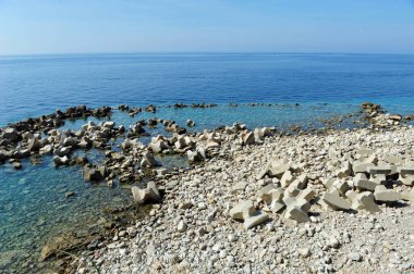 Kaya, kaya ve dalga kırıcı taşların karışımı. Arka planda mavi deniz ve gökyüzü olan yatay bir fotoğraf. Boşluğu kopyala.