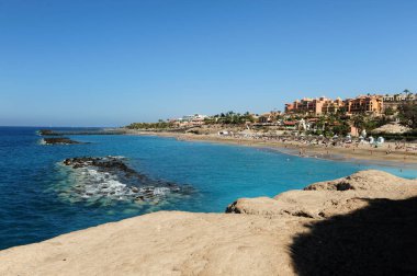 İspanya 'nın Tenerife adasındaki sahil ve otellere doğru kayalıklardan manzarayı izleyin. Turkuaz mavi okyanus ve insanlarla dolu kumlu plaj..