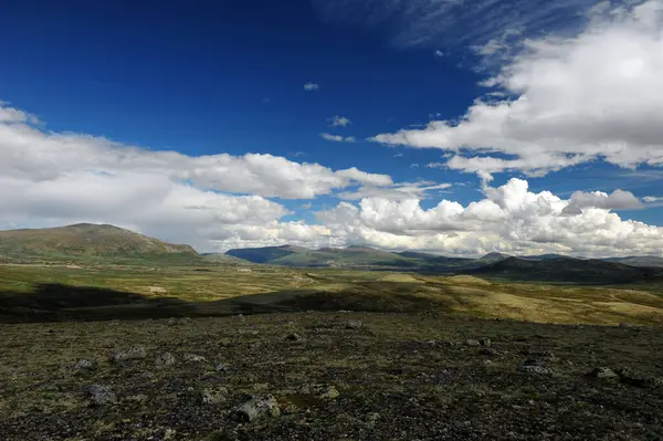 Norveç dağ manzarasında yere gölge düşüren bulutlar. Norveç 'te güzel bir dağ bölgesi güneşli bir günde mavi gökyüzü ve beyaz bulutlarla.  