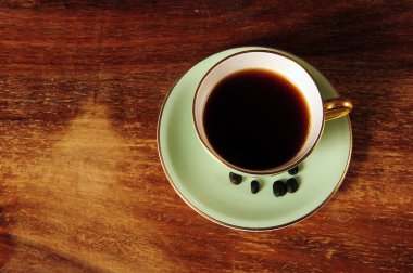 Eskimiş pastel yeşil fincan ve kahve çekirdekli çay tabağı çizik ahşap masa. Kahve ve güzel kahve fincanı. Fotokopi alanı solda olan yatay fotoğraf.