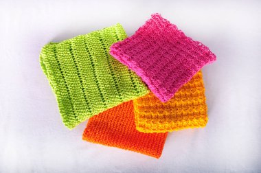 Four hand knitted dishcloths in multiple colors.  Cloths neatly folded in center of horizontal photo.  Copy space to the left and the right of image. clipart