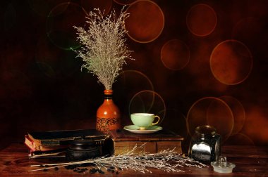 Eski kitapların, nane yeşili kahve fincanının, kahve çekirdekli bardağın ve seramik vazoda dekoratif kamışların yatay fotoğrafı. Kahve çekirdekleri ahşap masaya yayılmış..