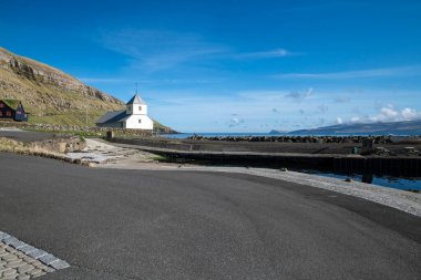 Faroe Adaları 'ndaki Kirkjuboeur' da güneşli bir günde beyaz taş kilisenin güzel manzarası. Mavi gökyüzü ve kıyı boyunca birkaç bulut.