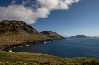 Mavi gökyüzü ve beyaz bulutlarla güneşli bir günde Faroe Adaları 'nın volkanik deniz manzarası. Sahil boyunca ilkbahar.