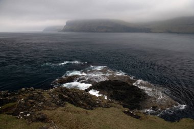 Faroese dağlarının üzerinde sis var. Bulutlu bir günde deniz manzarası. Kopyalama alanı olan yatay fotoğraf.