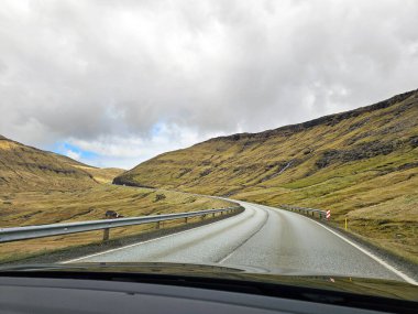 Araba penceresinden yol manzarası. Faroe Adaları 'nın virajlı yollarında güzel manzaralar, değişen hava koşullarıyla dolu bir günde. 