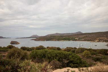Sakin kıyı manzarası sakin mavi denizle buluşan kayalık uçurumların çarpıcı görüntüsü, sularda süzülen yelkenliler yumuşak bulutlu bir gökyüzü altında, Yüksek kalite fotoğraf