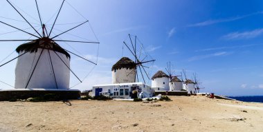 Mikonos adasında bulutlu gökyüzünün altında geleneksel Yunan yel değirmenleri. Yunanistan 'ın Cyclades kentindeki ikonik Mykonos yel değirmenlerinin hava görüntüsü. Seyahat ve mimari konsepti. Yüksek kalite fotoğraf