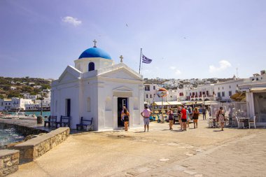 1 Eylül 2023, Mykonos, Yunanistan. Yunanistan 'ın Mykonos kentinde güneşli bir günde mavi kubbeli ve Yunan bayrağıyla beyaz kilise. Seyahat ve mimari konsepti. Yüksek kalite fotoğraf