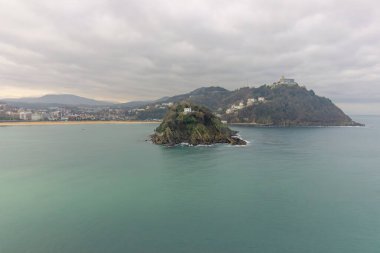 Santa Clara Adası ve Monte Igueldo 'nun turkuaz suları ve San Sebastian, İspanya' da bulutlu bir gökyüzünün altındaki kıyı şehri manzarası. Yüksek kalite fotoğraf