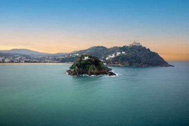 Santa Clara Adası ve Monte Igueldo 'nun turkuaz suları ve San Sebastian, İspanya' da bulutlu bir gökyüzünün altındaki kıyı şehri manzarası. Yüksek kalite fotoğraf