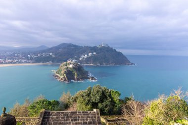 Santa Clara Adası ve Monte Igueldo 'nun turkuaz suları ve San Sebastian, İspanya' da bulutlu bir gökyüzünün altındaki kıyı şehri manzarası. Yüksek kalite fotoğraf