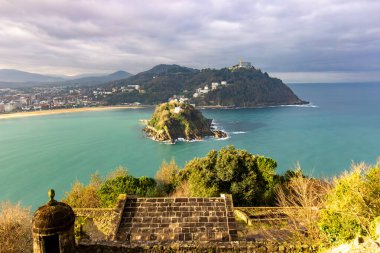 Santa Clara Adası ve Monte Igueldo 'nun turkuaz suları ve San Sebastian, İspanya' da bulutlu bir gökyüzünün altındaki kıyı şehri manzarası. Yüksek kalite fotoğraf
