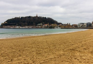 San Sebastian, İspanya 'da gün batımında kıyıya yakın binaları ve arka planında tepeleri olan kumsal. Kıyı kenti ve doğal manzara. Yüksek kalite fotoğraf