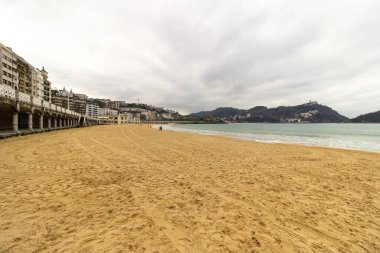 San Sebastian, İspanya 'da gün batımında kıyıya yakın binaları ve arka planında tepeleri olan kumsal. Kıyı kenti ve doğal manzara. Yüksek kalite fotoğraf