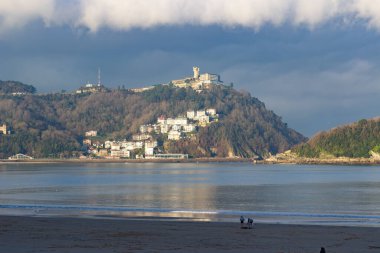 San Sebastian, İspanya 'da gün batımında kıyıya yakın binaları ve arka planında tepeleri olan kumsal. Kıyı kenti ve doğal manzara. 