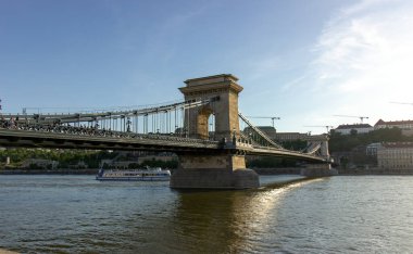 Budapeşte 'deki Zincir Köprüsü' nün yan görüntüsü Tuna Nehri 'ni asma kabloları, taş sütunlar ve altından geçen bir turist teknesi ile kaplıyor.. 