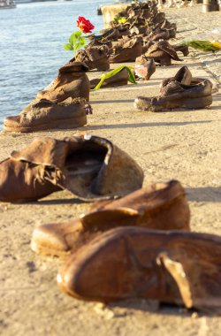Budapeşte 'deki Danube Bank Anıtı' nın yakın ve geniş manzaralı nehir kenarındaki gezinti alanı boyunca bronz ayakkabılar, çiçekler ve mumlarla.