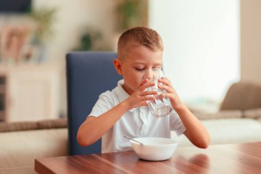Evde kahvaltı yapan, suyla yulaf lapası yiyen 5 yaşında tatlı bir çocuk. Doğal ışık, sağlıklı yiyecekler, yemek masasındaki çocuk, sıcak aile anı..