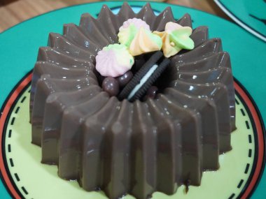 Yeşil tabakta çikolatalı pudingi yakın plan. Puding koyu kahverengi ve pürüzsüz. Pudingin üstünde bir sürü Oreo kurabiyesi ve renkli şekerlemeler vardı.