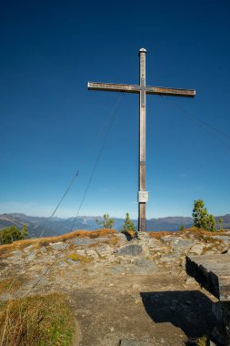 Avusturya Alpleri 'nde Gerlosstein' in tepesinde tahta haç. Sonbaharın güneşli bir gününde arkada dağ manzarası ve mavi gökyüzü. Güneşli bir günde dağın tepesinde