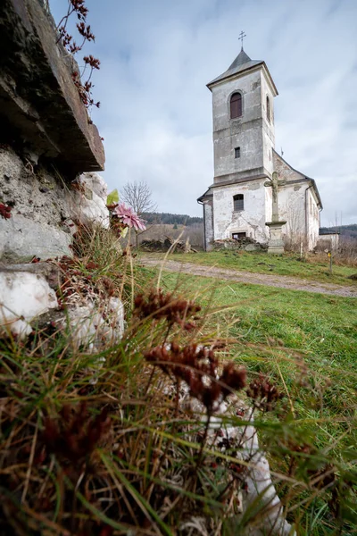 Vertical shot of old Church of Saint John of Nepomuk falling apart on a warm cloudy day of winter with stones and grass in front