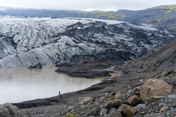 アイスランド南部の寒い曇り空の日に氷河によって浚渫された赤と青の屋外ジャケットの人々 曇った寒い日に氷河が氷河のラグーンに落ちる — ストック写真