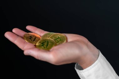 Kadın eli, siyah arka planda birkaç altın bitcoin tutuyor. Bitcoin büyümesi, değer biçimi, finansal kazanç, boğa pazarı, kripto para biriminin yükselişi kavramı