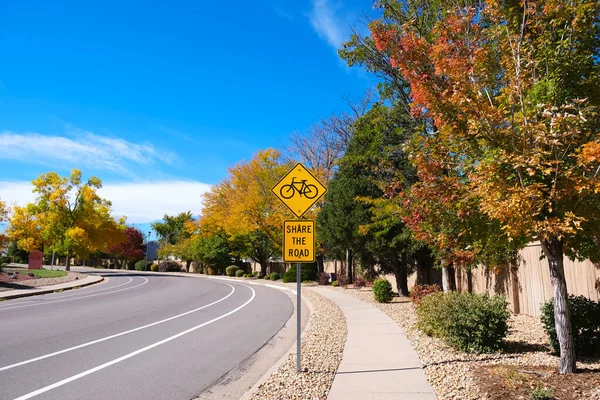Yellow diamond warning road sign with bicycle symbol and Share the road text along empty curved road inside residential city area with bright blue sky,yellow trees street view autumn landscape photo