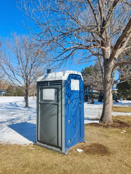 Blue portable restroom cabin in local park in bright winter day vertical photo. Porta-potty public toilet.