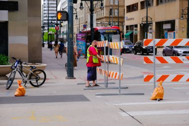 Denver, USA - May 05, 2024: Worker setting up a barrier for a street closure due to a city festival event with orange and white barricades, a bicycle, and a traffic light at an urban intersection. clipart