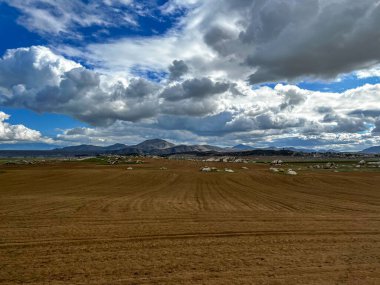 Açık arazi tarlası, güzel bulutlar, arkasında dağlar.