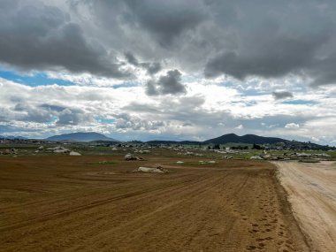 Açık arazi tarlası, güzel bulutlar, arkasında dağlar.