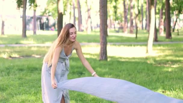 夏の服を着た女性が緑の芝生の上にスカーフを置き 公園でリラックスするために座っています スローモーション 4K映像 — ストック動画