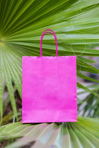 ヤシの葉の上にピンクの明るい紙の袋を閉じます モックアップ — ストック写真
