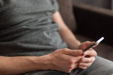 Elinde cep telefonuyla kanepede oturan bir adam. Evde dinleniyorum.