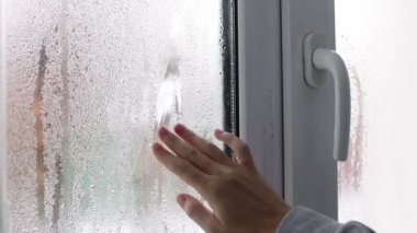 A womans hand touching wet window glass with water drops of condensation. 4k footage