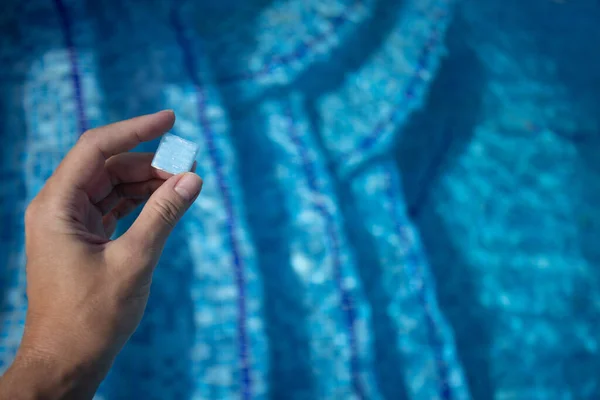 Hand holding small tile from floor of swimming pool. Design of the swimming pool