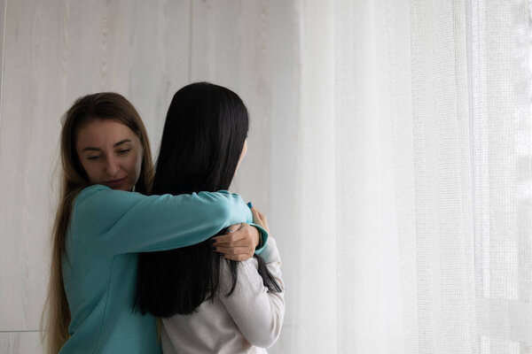 Two best girlfriends hugging embracing near window at home