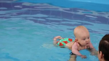 Antrenör yüzme havuzunda gülümseyen bebek. Koç yeni doğmuş bebeği tutuyor, suya dalmayı öğretiyor. Koç yardımıyla yüzmeye çalışan küçük bir çocuk. 4k görüntü. 