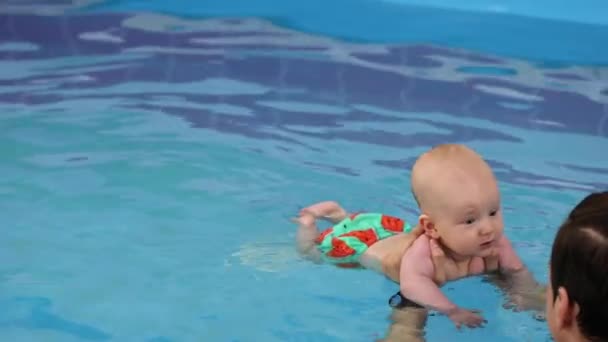 トレーナーのプールで笑顔の赤ちゃん コーチは新生児を抱え 水の下で潜ることを教えています コーチの助けを借りて泳ごうとする小さな子供 4K映像について — ストック動画