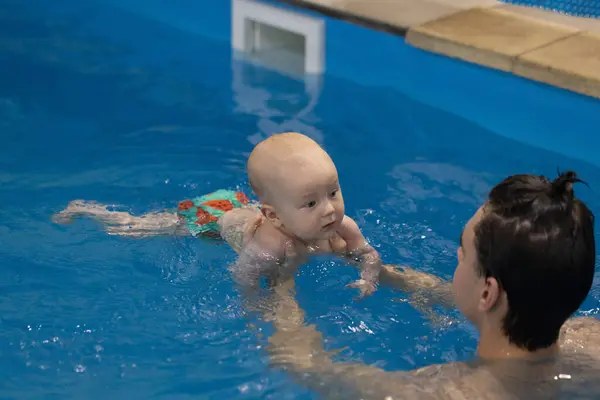 Baby looking with interest to the swim coach. Swim coach holding newborn, teaching to swim.