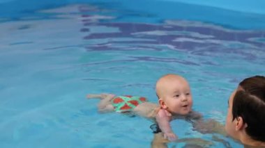 Antrenör yüzme havuzunda gülümseyen bebek. Koç yeni doğmuş bebeği tutuyor, suya dalmayı öğretiyor. Koç yardımıyla yüzmeye çalışan küçük bir çocuk. 4k görüntü. 