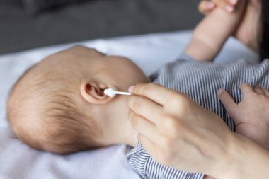 Bir bebeğin kulağına pamuklu çubuk sokulmuş bir kadın eli. Yakın çekim.