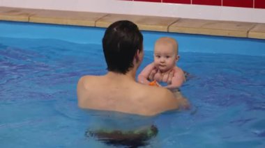Elinde oyuncakla bir yüzme hocasıyla yüzen yeni doğmuş rahat bir bebek. 4k görüntü