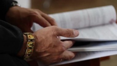 Rahibin elinde azizlerle birlikte bileklik. Siyah cüppeli rahip Hıristiyanlıktan önce azizlerin isimlerini okuyordu. Seçici odaklanma. Tam HD görüntüler